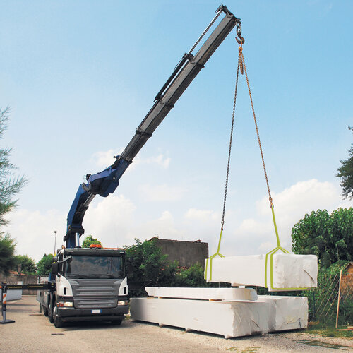 Lkw liefert Holzpakete Ein Lkw mit einem Teleskopkran setzt Holzpakete vor einem Zaun ab.