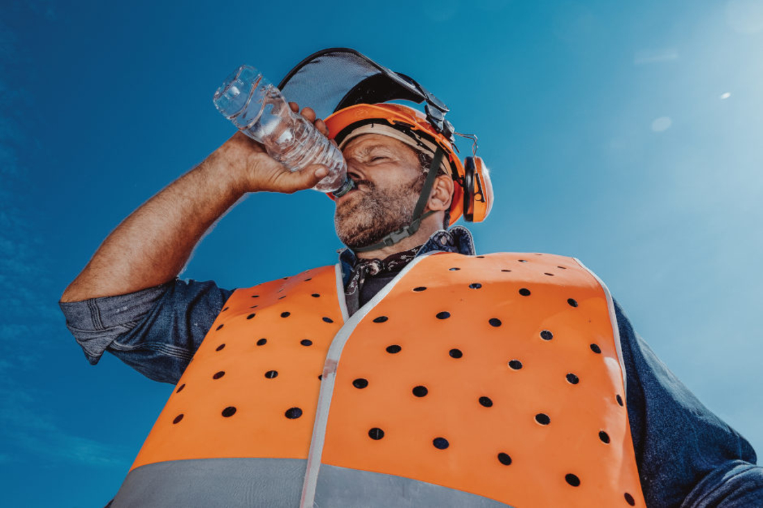 Bauarbeiter mit Schutzhelm und Sicherheitsweste trinkt aus einer Wasserflasche. – Bild: patrickjohn71